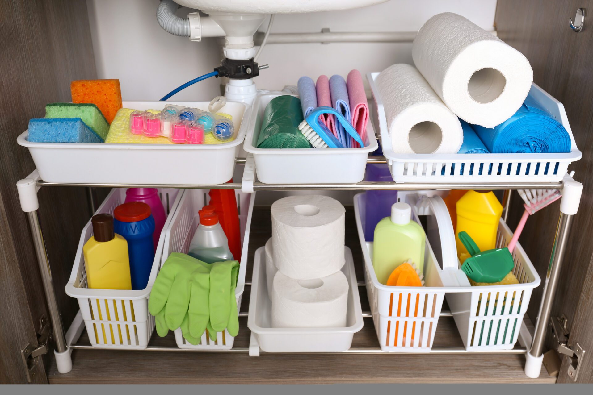 Organized cleaning supplies and toilet paper in baskets under a sink.